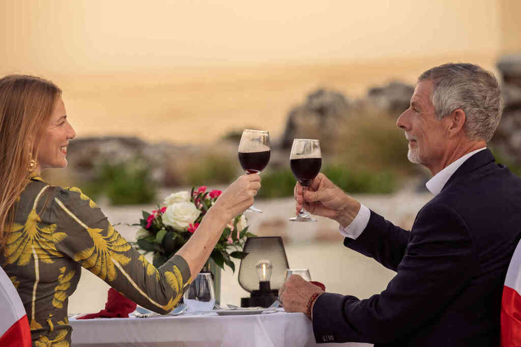 A couple clinks wine glasses together at an outdoor table, celebrating a special moment in a scenic setting.