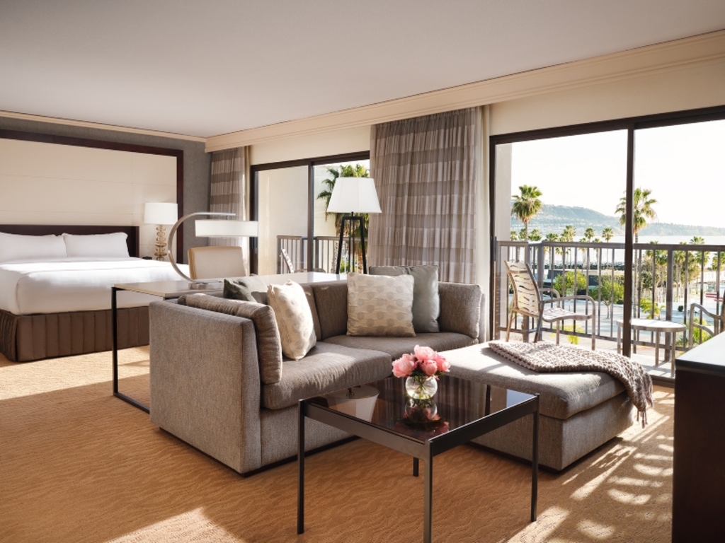 A hotel room featuring a bed, a couch, and a balcony with a view of the ocean.