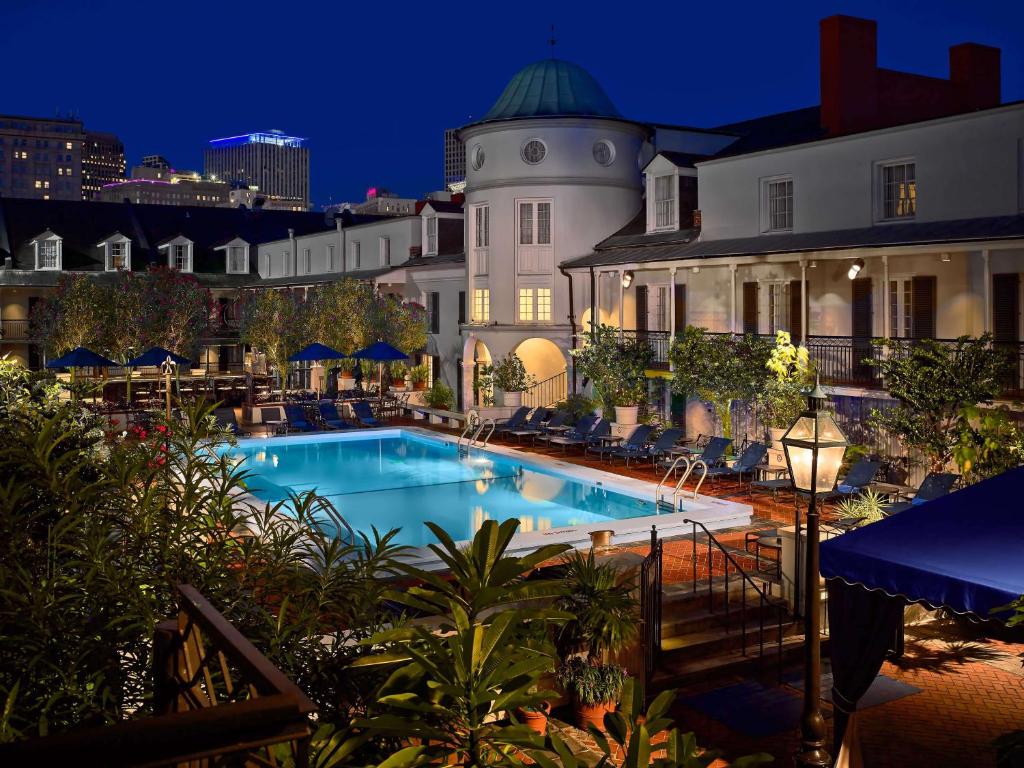 The hotel pool illuminated at night, surrounded by palm trees and lounge chairs under a starry sky.