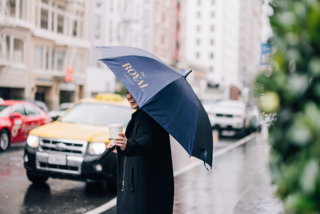 A woman stands in the rain, holding a colorful umbrella to shield herself from the downpour.