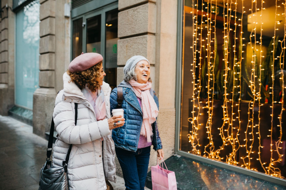 Two women stroll down a festive street adorned with colorful Christmas lights, creating a cheerful holiday atmosphere.
